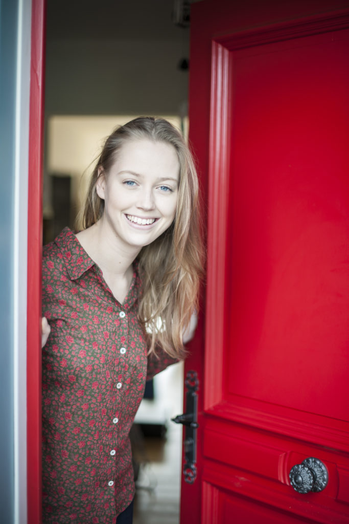 Beautiful,Young,Woman,Opening,A,Red,Door,To,Welcome,Someone