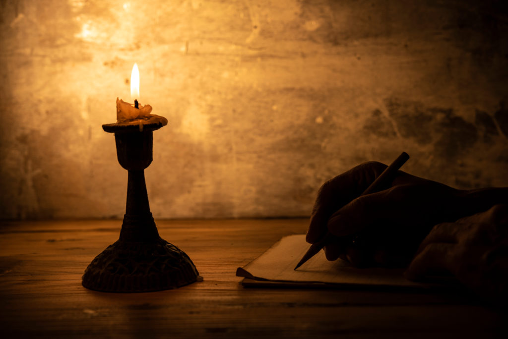 Hand,Writing,Letter,With,Pencil,On,Paper,In,Candle,Light