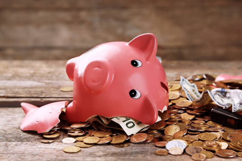Broken,Piggy,Bank,With,Cash,And,Coins,On,Wooden,Background