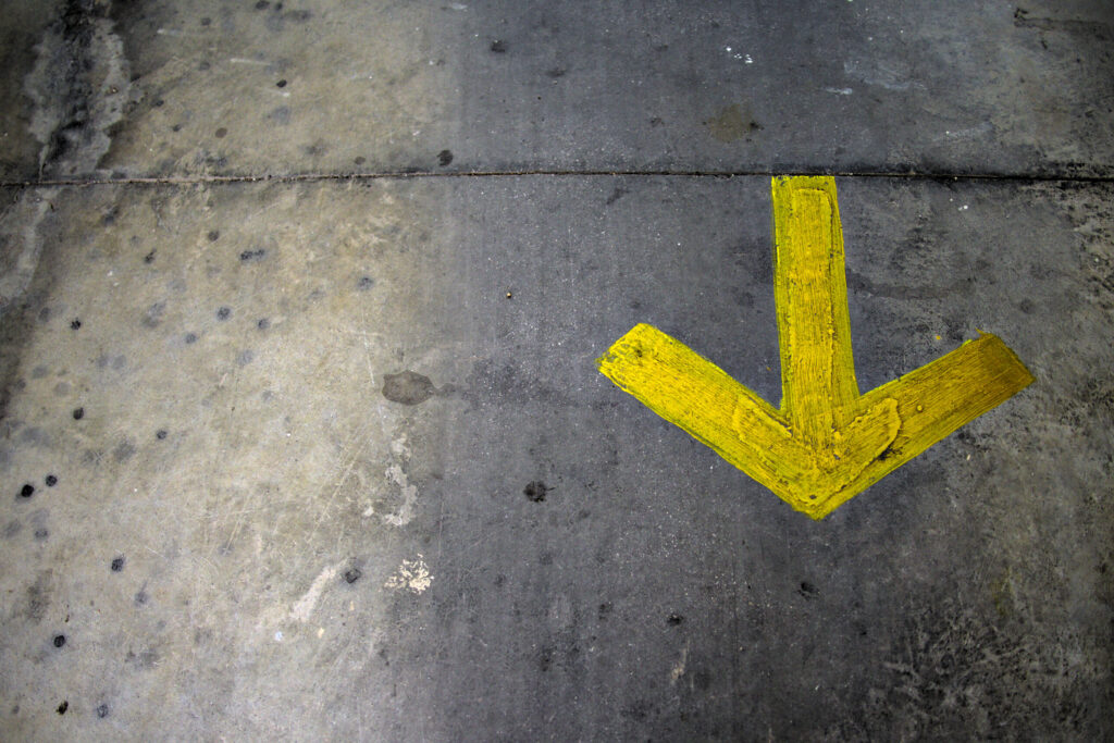 Vibrant,Yellow,Arrow,Pointing,Down,On,Textured,Asphalt,Background.