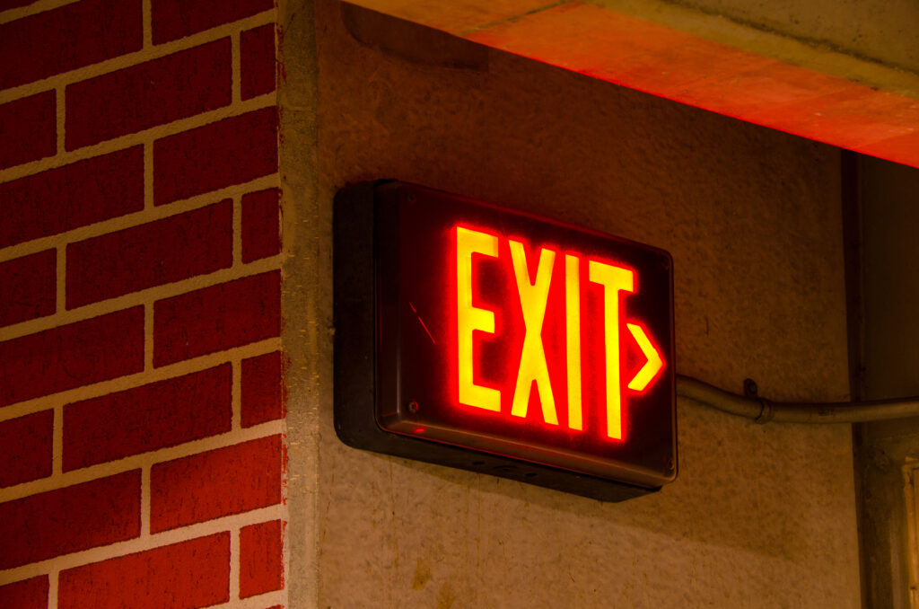 Glowing,Electrical,Exit,Sign,Mounted,On,A,Brick,Concrete,Wall